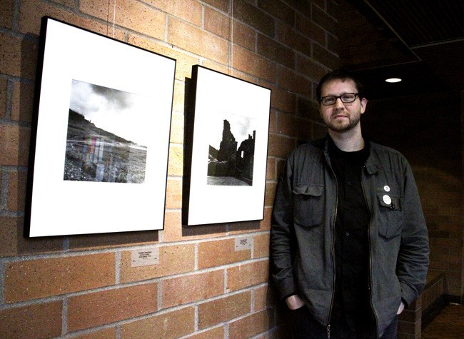 Green River Community College staffer Zach Kolden poses in front of a pair of prints at his city hall exhibit.