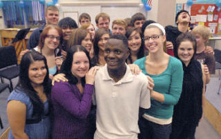 Mukisa Willy is surrounded Jon Stenson’s Vocal Jazz Ensemble at Auburn Riverside High School. The group is conducting a benefit concert for Willy.